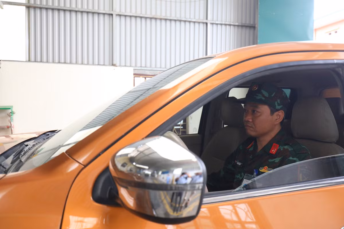 Phía trong dây chuyền, 1 kiểm định viên quân sự khác được phân công kiểm tra gầm, hỗ trợ việc di chuyển xe trên dây chuyền để thực hiện công đoạn kiểm tra đèn xe, trong khi kiểm định viên quân sự còn lại phụ trách việc chụp ảnh lưu trữ tem kiểm định xe lên hệ thống cơ sở dữ liệu và thực hiện việc dán tem kiểm định giúp người dân.