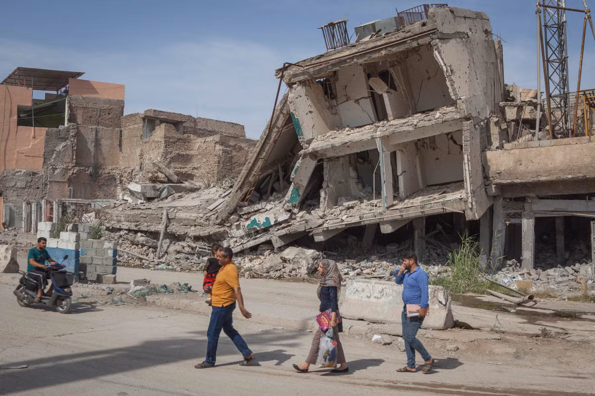 Người dân đi qua những ngôi nhà đổ nát ở Mosul.