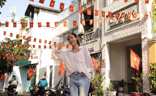 Các khu chung cư như Trần Nhật Duật, Nguyễn Huệ (quận 1) cũng trang hoàng cờ hoa, băng rôn từ hành lang đến ban công, tạo nên một khung cảnh sống động với sắc đỏ rực rỡ nổi bật giữa những mảng tường. (Ảnh: Du khách tranh thủ check in trên một con hẻm rợp cờ tại quận 1).