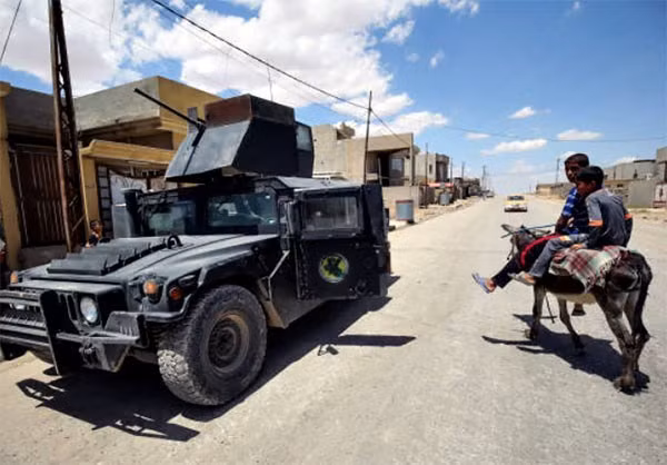 Hai em nhỏ đi qua chiếc xe quân sự của quân đội Iraq trên đường phố Mosul. Ảnh: FNA.