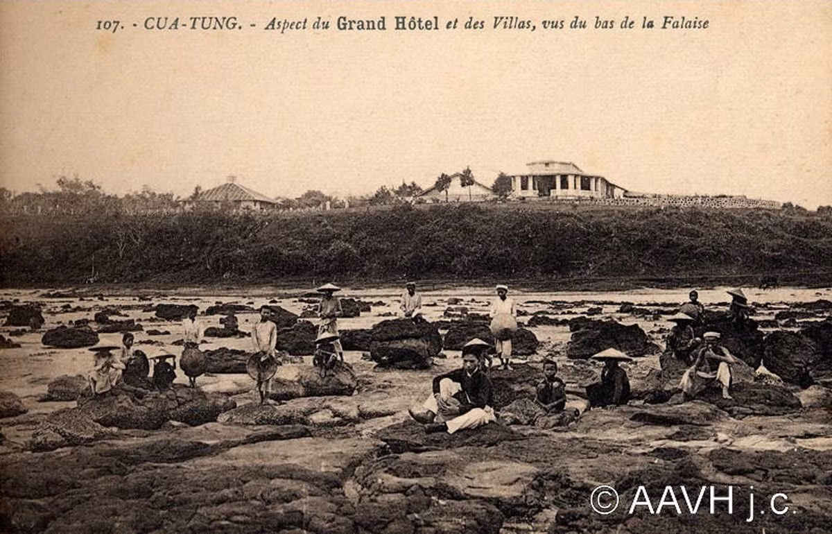 Người lao động bản xứ ngồi nghỉ ở bãi đá trên bờ biển Cửa Tùng, 1930. Phía xa là khách sạn Grand. Ảnh: Aavh.org.