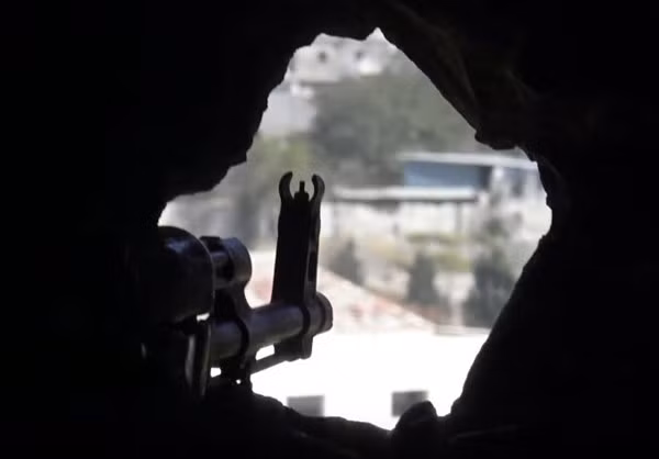 Họng súng của một binh sỹ Syria ngắm qua lỗ châu mai ở công sự.
