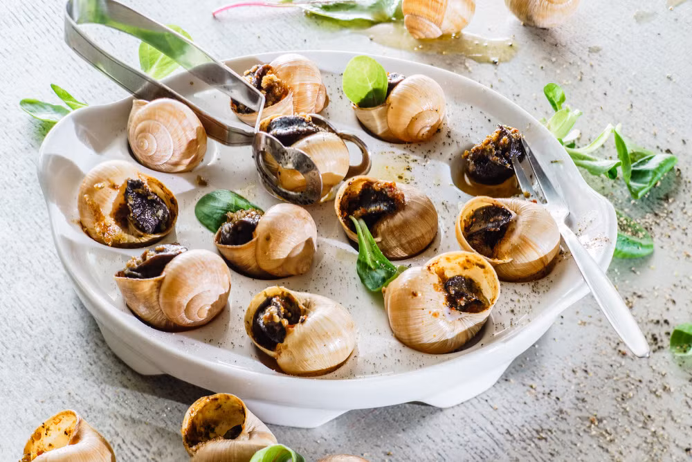 Do dùng cả vỏ để trình bày món ốc sên nên đầu bếp cũng phải làm sạch chúng một cách cẩn thận. Tại một số quốc gia, vỏ ốc sên được thay thế bởi những chiếc bánh ngọt nhỏ nhiều lớp (puff pastry). Như vậy trông món ăn vệ sinh hơn nhưng bánh ngọt lại ngấm bơ và làm mất sự thú vị khi thưởng thức ốc sên. Ảnh: Vivial.