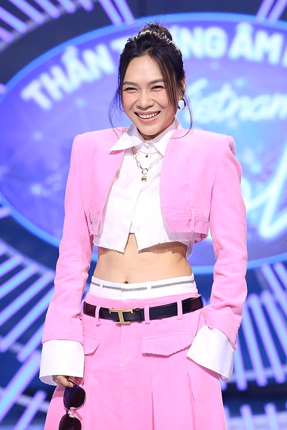 Mỹ Tâm ‘biến hoá’ phong cách với trang phục tông hồng, trắng phong cách Barbie. Nữ ca sĩ tiếp tục diện blazer không cổ, độn vai, dáng lửng làm từ nhung tăm, bên trong là sơ mi crop-top trắng khoe vòng eo thon gọn. ‘Hoạ mi tóc nâu’ thể hiện cá tính với váy dài ton-sur-ton cạp trễ phối cùng boot đen đế dày và thắt lưng có mặt khóa hình chữ T.