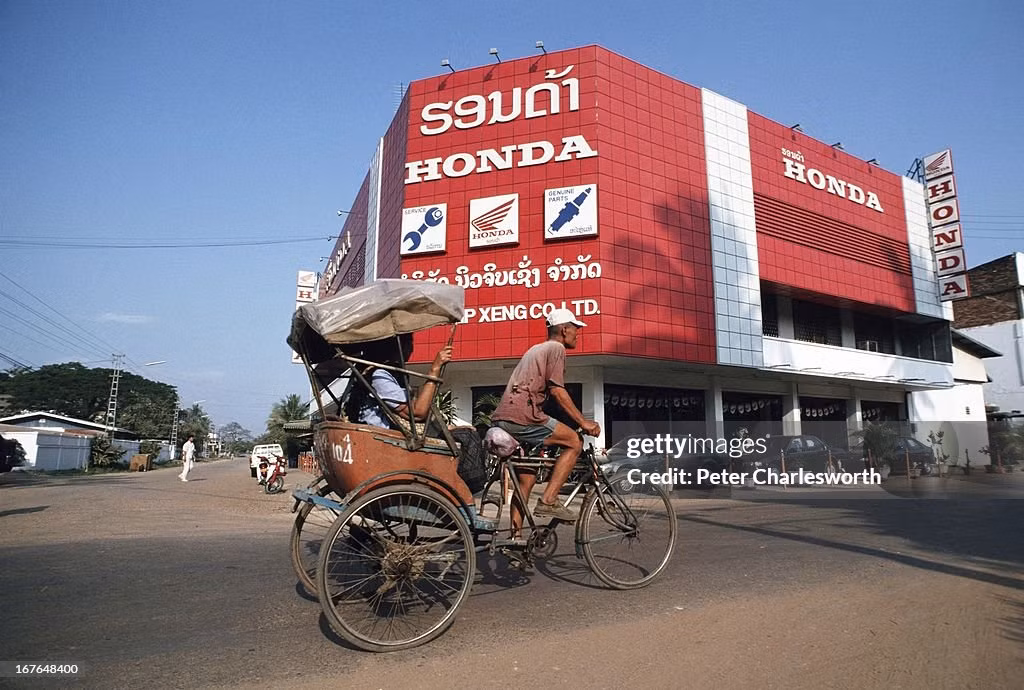 Người đạp xích lô chở khách đi ngang qua đại lý duy nhất của hãng xe máy Honda ở Vientiane.