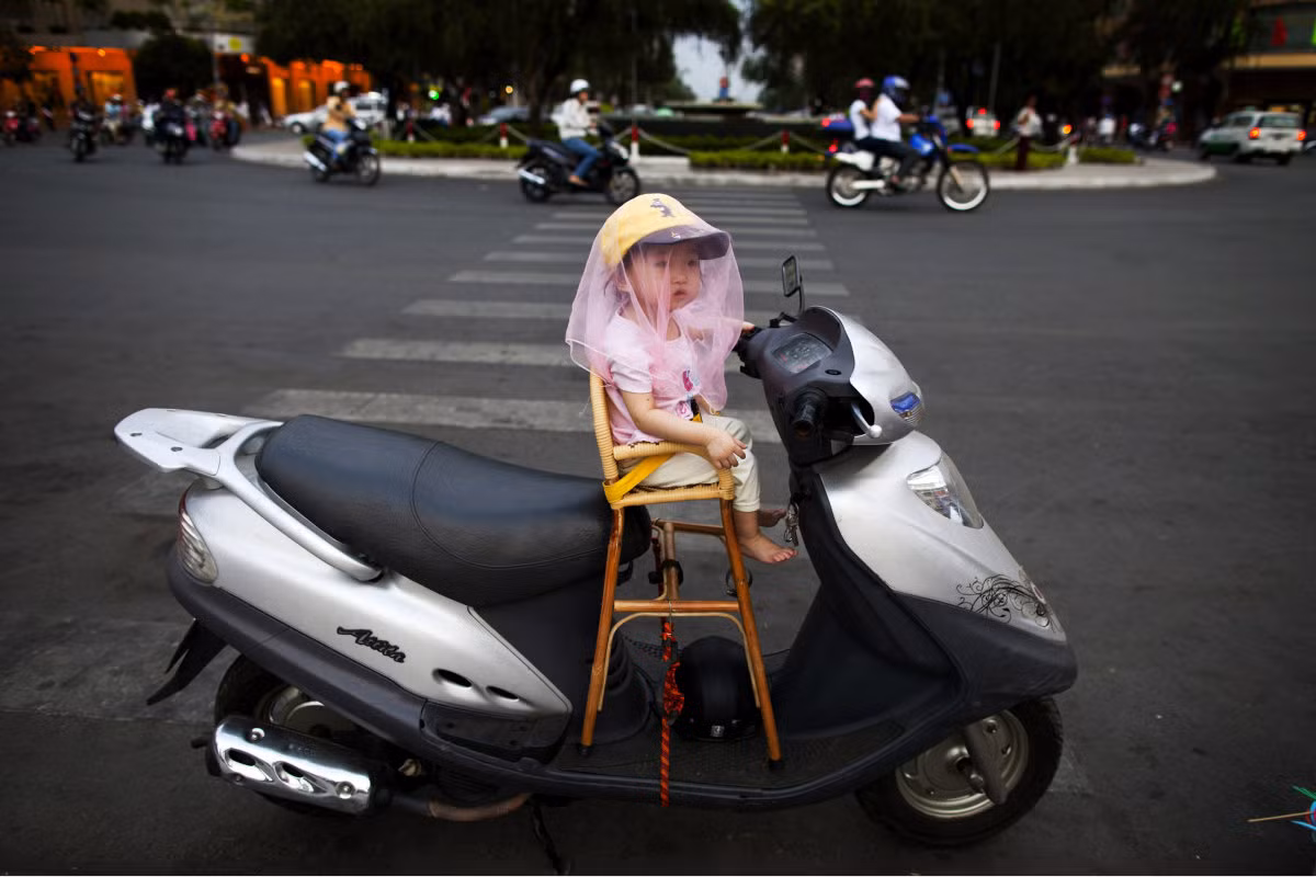 Em bé ngồi trên ghế tựa gắn trên xe máy trong lúc bố em đang chạy đi mua đồ. Ảnh USN