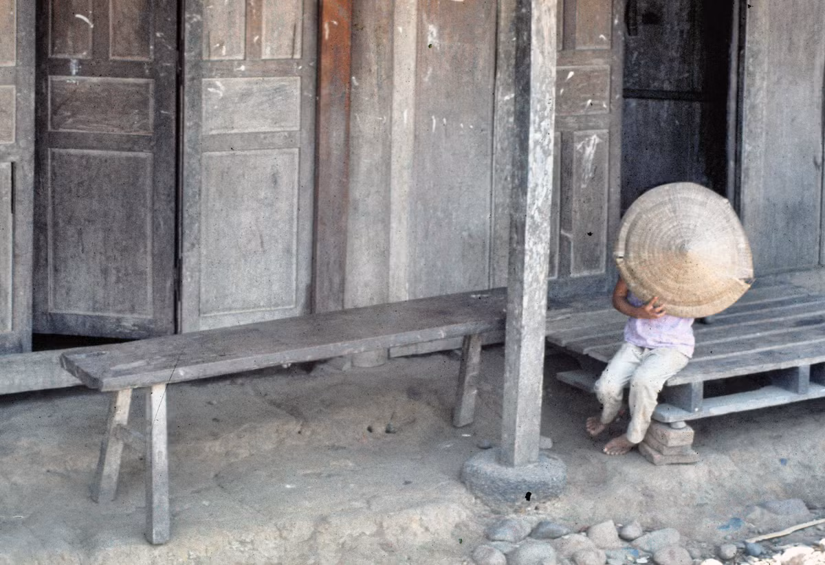 Em bé bên hiên nhà lấy nón che mặt khi được chụp hình. Ảnh: Edward Palm.
