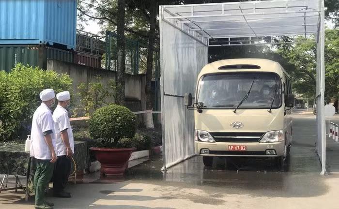 Cụ thể, đoàn xe chở công dân từ sân bay về sẽ được sát khuẩn tại cổng sư đoàn, sau đó người dân xuống xe và thực hiện tuần tự các bước gồm nhận kính và khử khuẩn tay, đi qua buồng khử khuẩn. Tiếp đó là bàn bỏ kính, sau đó tới bàn cấp khẩu trang và khử khuẩn tay, kế tiếp qua bàn kiểm tra thân nhiệt và nhận tờ khai y tế. Sau đó là khu vực kê khai y tế. Khoảng 9 giờ, xe chở các công dân từ vùng dịch về đến Sư đoàn 317. Tại đây chiếc xe phải đi qua cổng sát khuẩn. Ảnh: MINH TÂM