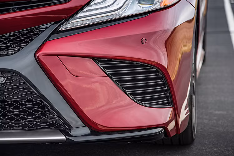 So với phiên bản cũ, Toyota Camry thế hệ mới được trang bị nắp capô nằm thấp hơn 40,6 mm. Riêng phiên bản hybrid của Toyota Camry 2018 đi kèm logo nằm giữa lưới tản nhiệt trên màu xanh dương như đặc điểm nhận dạng. Những đường gân bên sườn và chắn bùn trước/ sau mang đến thiết kế đậm chất thể thao cho Toyota Camry 2018.
