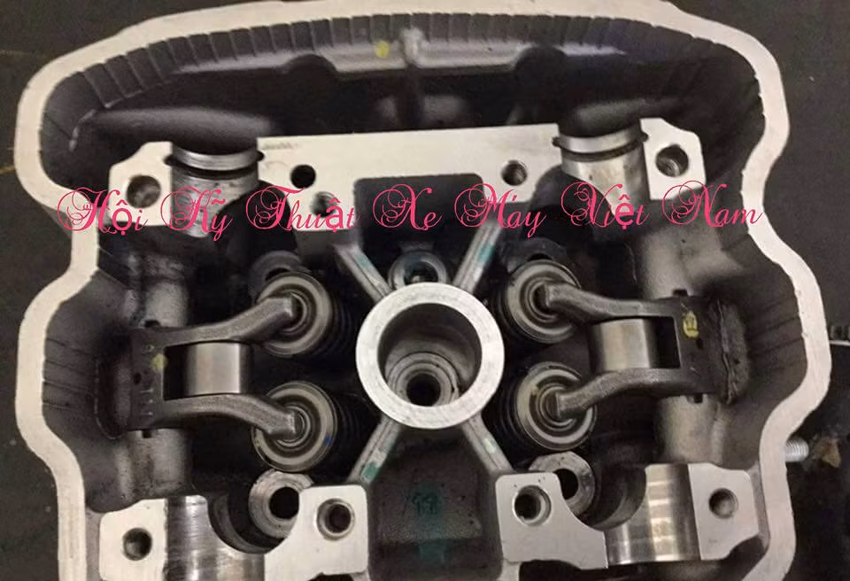 Trước tiên, chi tiết quen thuộc vài ngày gần đây chính là "đầu bò" DOHC tích hợp giảm ma sát, khối động cơ mới của Honda ở phân khúc 150 phân khối. Như vậy, chúng ta thấy rất rõ, có tất cả 2 cây cam nhưng trên mỗi cây cam chỉ có 1 gói cam, tì vào cây cò đẩy 2 cây xúp páp.
