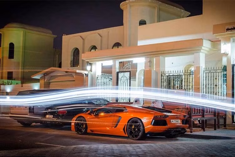 Chiếc siêu xe Lamborghini Aventador màu cam bên ngoài dinh thự của một người dân, bên cạnh là bộ đôi xe sang gồm Bentley và Land Rover.