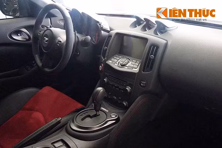 Bên trong khoang cabin, Nissan 370Z Nismo 2015 lấy màu đen làm chủ đạo đi cùng màu đỏ trên ghế ngồi, các đường chỉ khâu, cụm đồng hồ, nút Start/Stop và logo Nismo cạnh cần số.