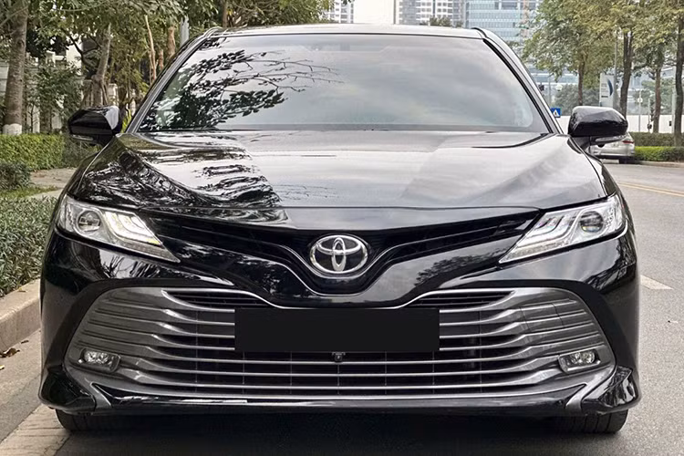 Về tổng thể, Toyota Camry 2019 đã qua sử dụng có kích thước dài x rộng x cao tương ứng là 4.885 x 1.840 x 1.445 (mm), chiều dài cơ sở đạt 2.825 mm và khoảng sáng gầm xe là 140 mm. Ở ngoại thất, đầu xe gây ấn tượng với cụm lưới tản nhiệt rộng kéo dài đến cản trước, đi kèm các thanh nhựa màu bạc nhũ xếp lớp.