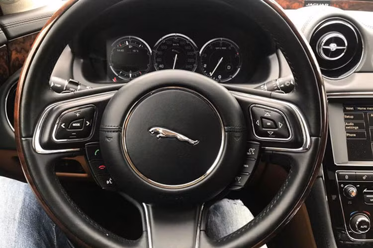 Vô-lăng trên mẫu xe sang Jaguar XJL là loại 3 chấu bọc da viền ốp gỗ tích hợp khá nhiều phím chức năng xử lý nhanh hỗ trợ người lái. Phía sau là bảng đồng hồ điện tử hiển thị thông số của xe có kích thước 12 inch.