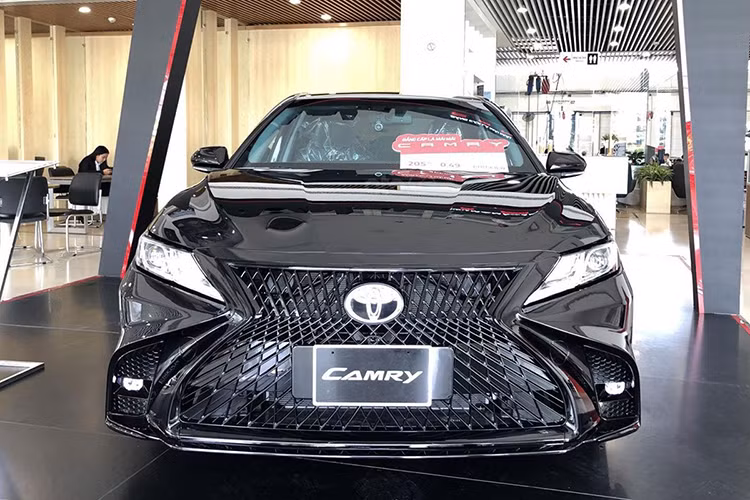 Phần đầu xe với trước nổi bật khi xuất hiện lưới tản nhiệt hình con suốt cỡ lớn đặc trưng của thương hiệu xe sang Lexus, nối liền cụm đèn chiếu sáng hình tứ giác nguyên bản của Camry. Bên dưới, cụm đèn sương mù của Toyota Camry độ Lexus nằm sâu trong hốc gió giả định cỡ lỡn. 