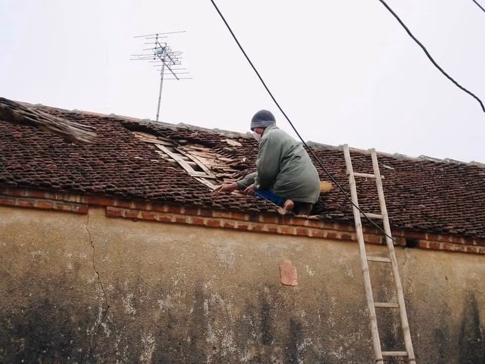 Hình ảnh một người đàn ông đang lợp lại mái nhà, phía sau là chiếc ăng-ten huyền thoại.