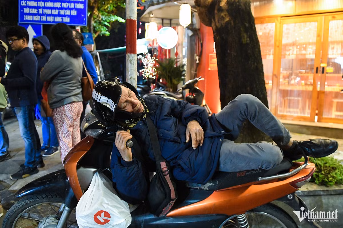 Đầu phố Lương Ngọc Quyến, một người lớn tuổi quàng khăn, đeo bịt tai, nằm lên yên xe máy trong bộ trang phục dày cộp.
