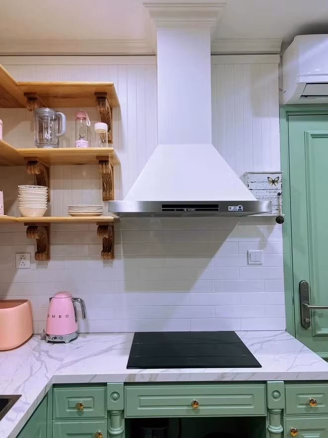 Khu bếp mang lại cảm giác nhẹ nhàng và tươi mới với gam trắng - xanh chủ đạo, được điểm xuyết bởi các món đồ bếp màu hồng và cam. Ảnh: FB Hòa Minzy