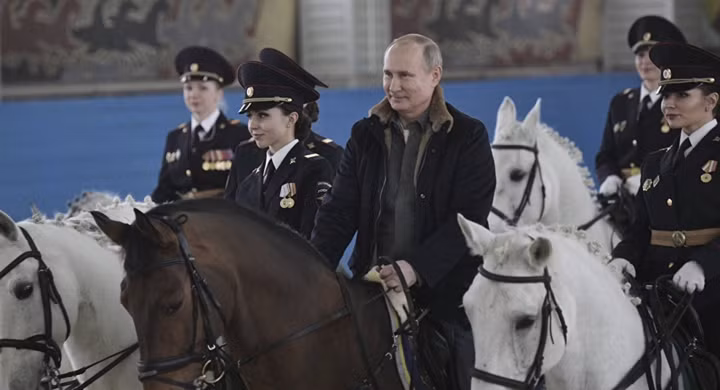 Tổng thống Nga Putin cưỡi ngựa sẫm màu, dẫn đầu đoàn nữ cảnh sát cưỡi ngựa trắng, chạy vòng tròn trong sân huấn luyện.