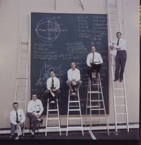 Các nhà khoa học NASA tạo dáng trước một tấm bảng đầy những phép tính phức tạp.