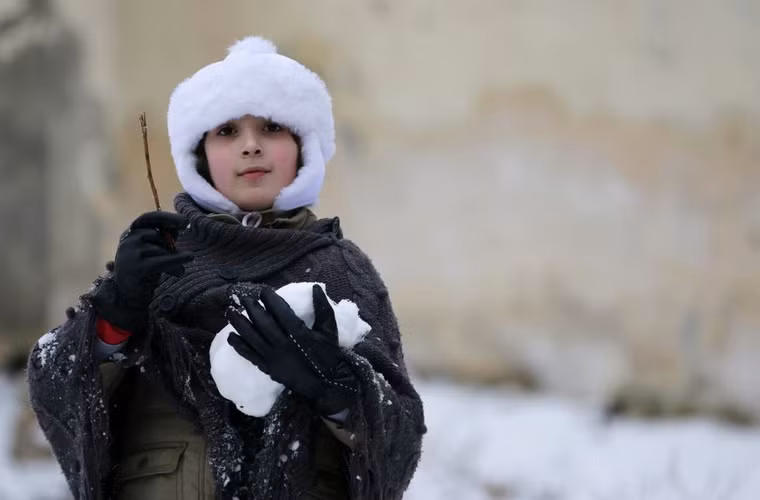 1 cô bé ôm quả cầu tuyết khi chơi đùa ở thành phố Aleppo, Syria ngày 11/1/2015. 