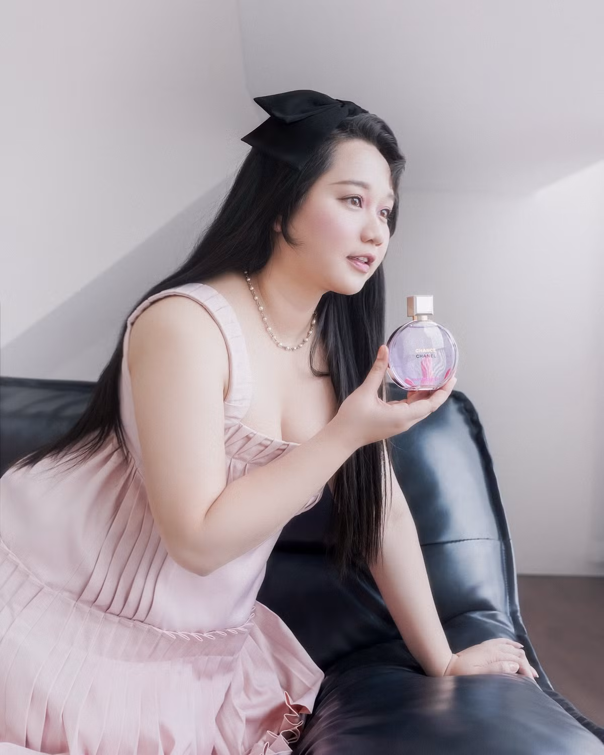 Điểm nhấn phụ kiện là chiếc nơ đen to bản trên mái tóc dài buông xoã, cùng chuỗi vòng cổ ngọc trai mang phong cách retro, tạo nên tổng thể hài hòa giữa sự trẻ trung và quý phái.