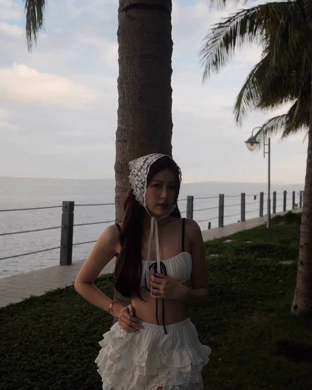 Chiếc mũ trùm đầu bằng ren trắng thắt nơ là phụ kiện tạo nên sự khác biệt. Phong cách vintage này đang trở lại mạnh mẽ và mang đến cho người mặc vẻ cổ điển, tiểu thư. Cùng với đó, chiếc túi cói cầm tay tăng thêm cảm giác mùa hè, hoàn thiện outfit theo phong cách "beach chic" một cách trọn vẹn.