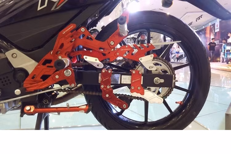 Bên còn lại, bản độ Suzuki Raider màu đỏ đen còn có thêm chống văng xích cùng hàng loạt các phụ kiện khác.